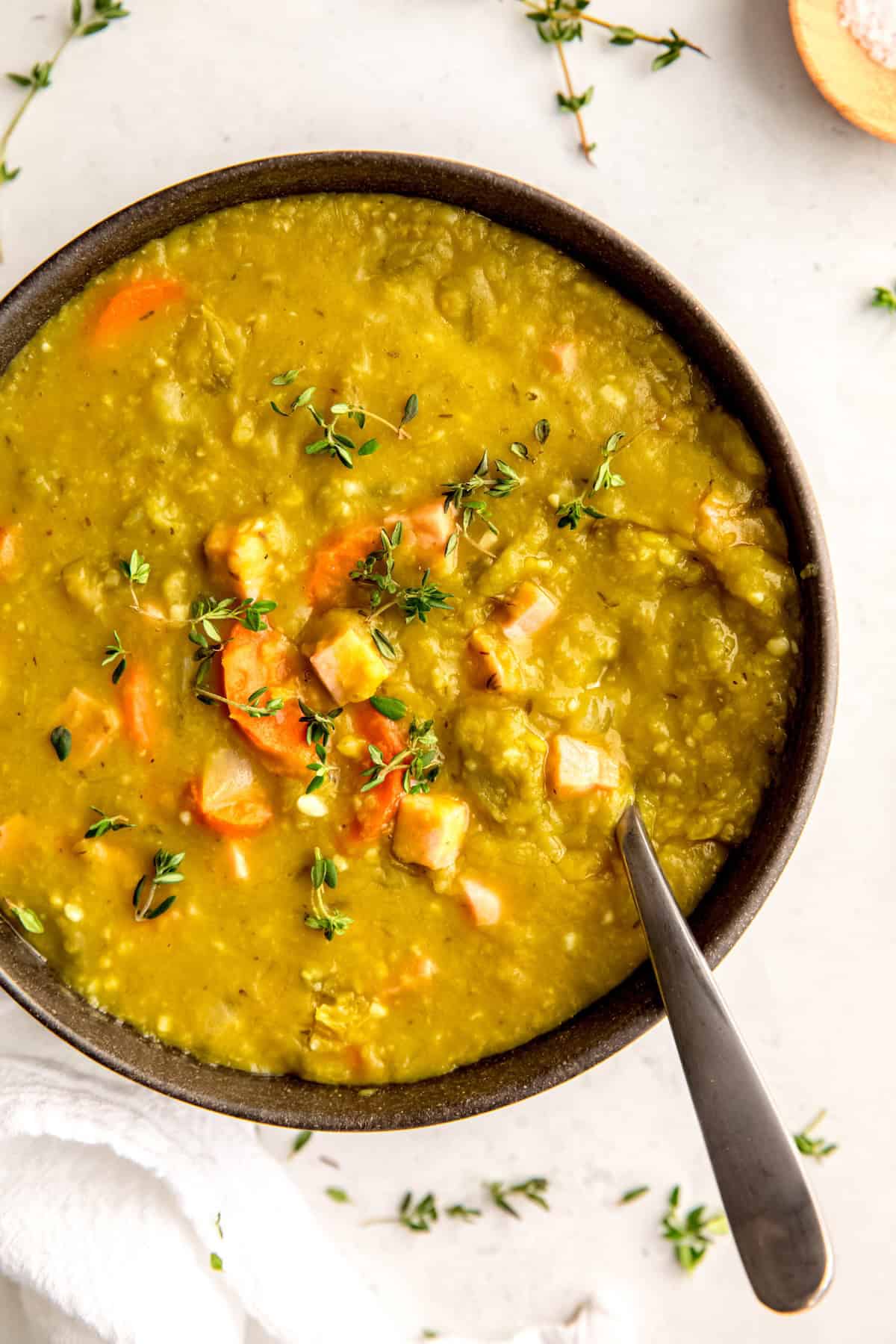 black bowl of instant pot split pea soup with ham garnished with fresh thyme leaves.