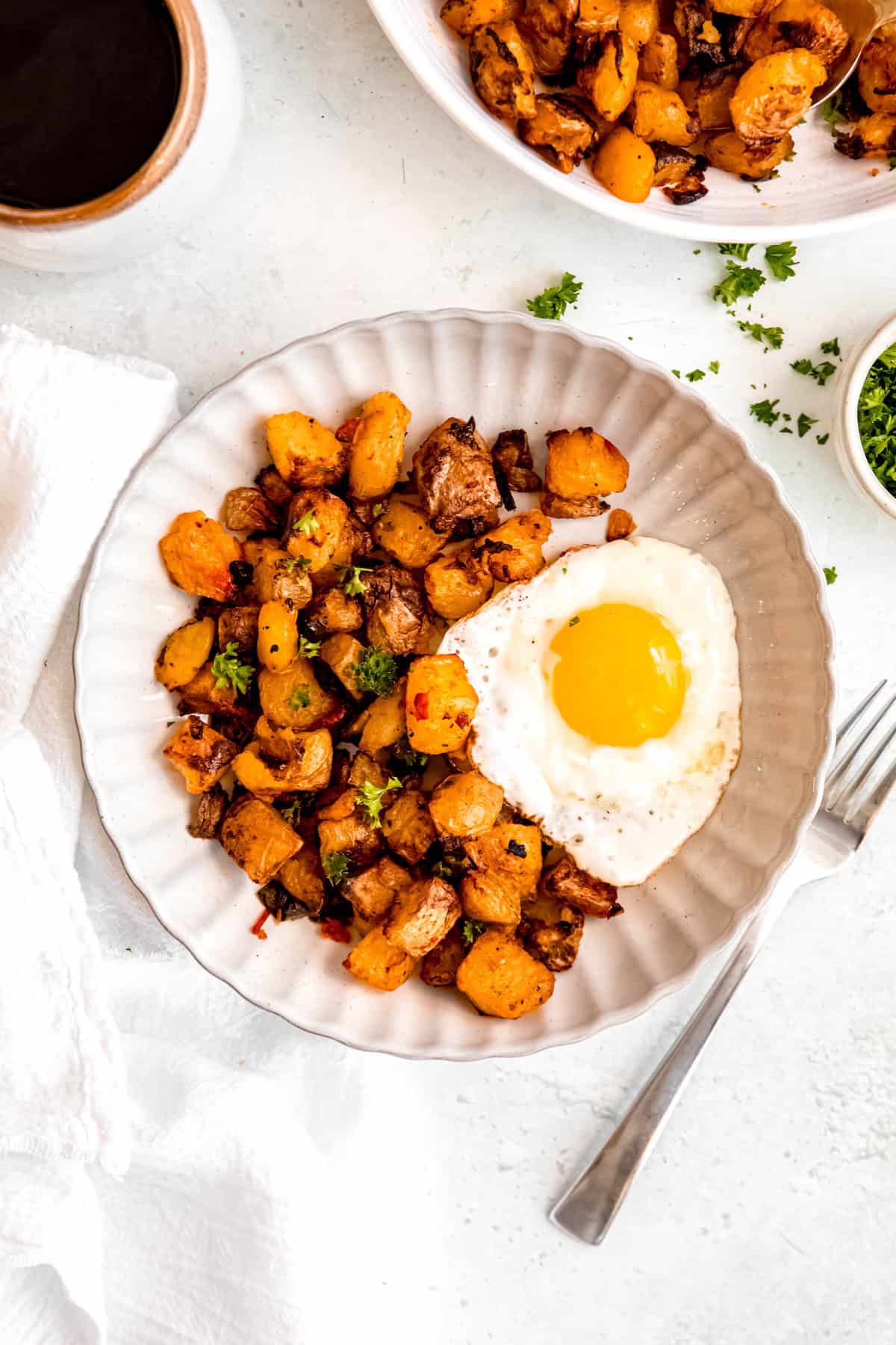 closeup overhead shot of a bowl of oven baked home fries with a sunny side up egg sprinkled with fresh parsley.