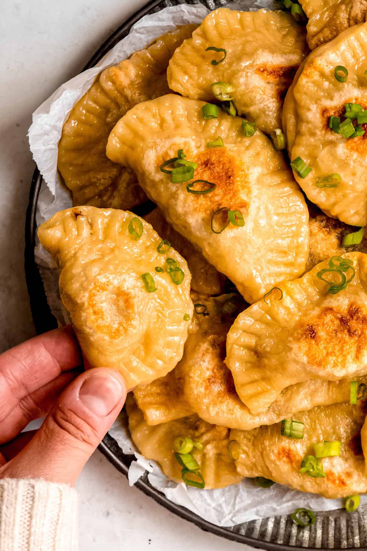 closeup shot of a hand in a white sweater up to the knuckles choosing a pan fried polish pierogi from the serving platter.