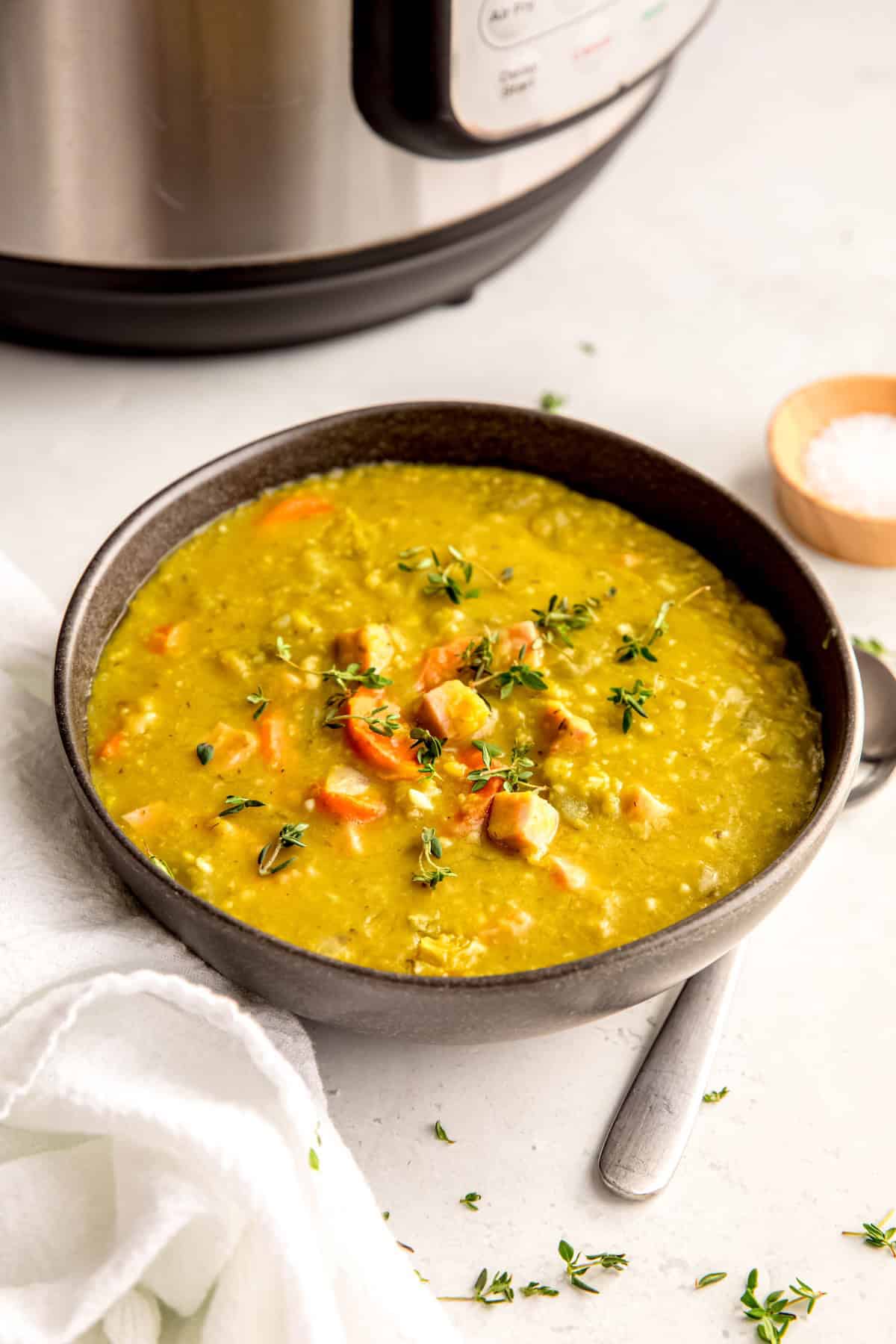 bowl of split pea ham bone soup garnished with fresh thyme leaves in front of an instant pot.