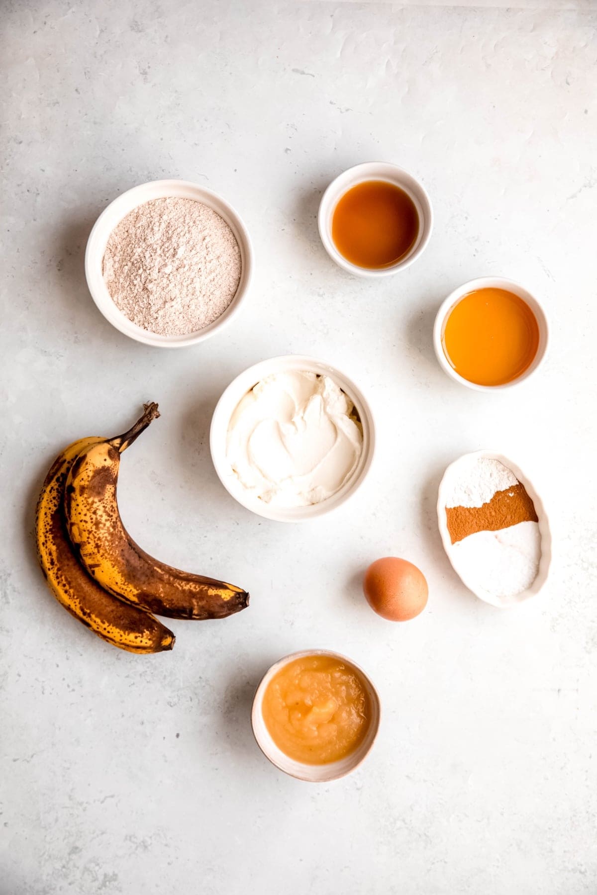 ingredients needed to make healthy whole wheat banana bread muffins measured out on a white table.