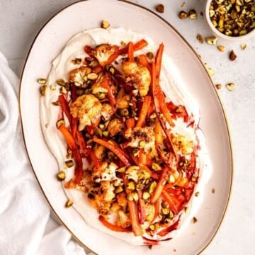 square hero image of harissa roasted carrots and cauliflower on a white oval serving platter.