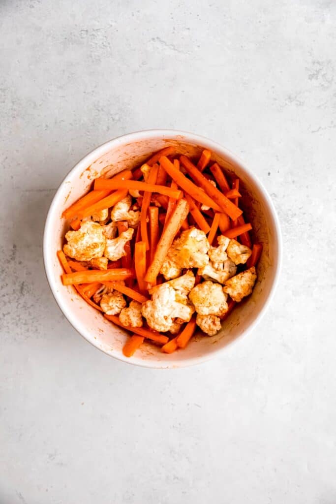 carrots and cauliflower in a mixing bowl after tossing with harissa and other seasonings.