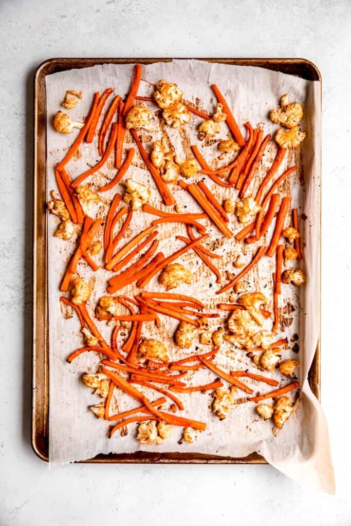 harissa roasted carrots and cauliflower on a parchment lined baking sheet.