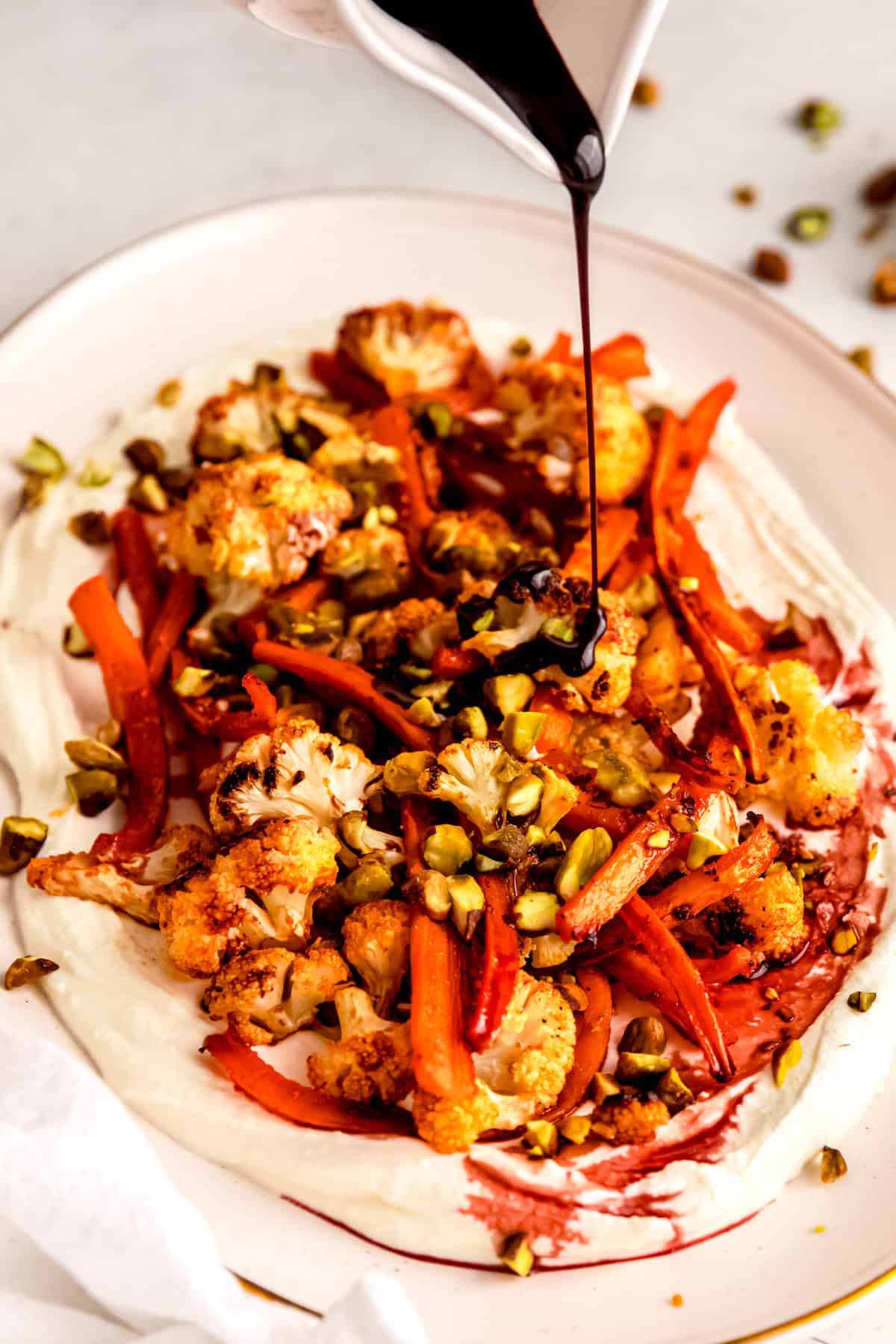 action shot of pomegranate molasses being drizzled on a bed of roasted carrots and cauliflower with whipped feta.