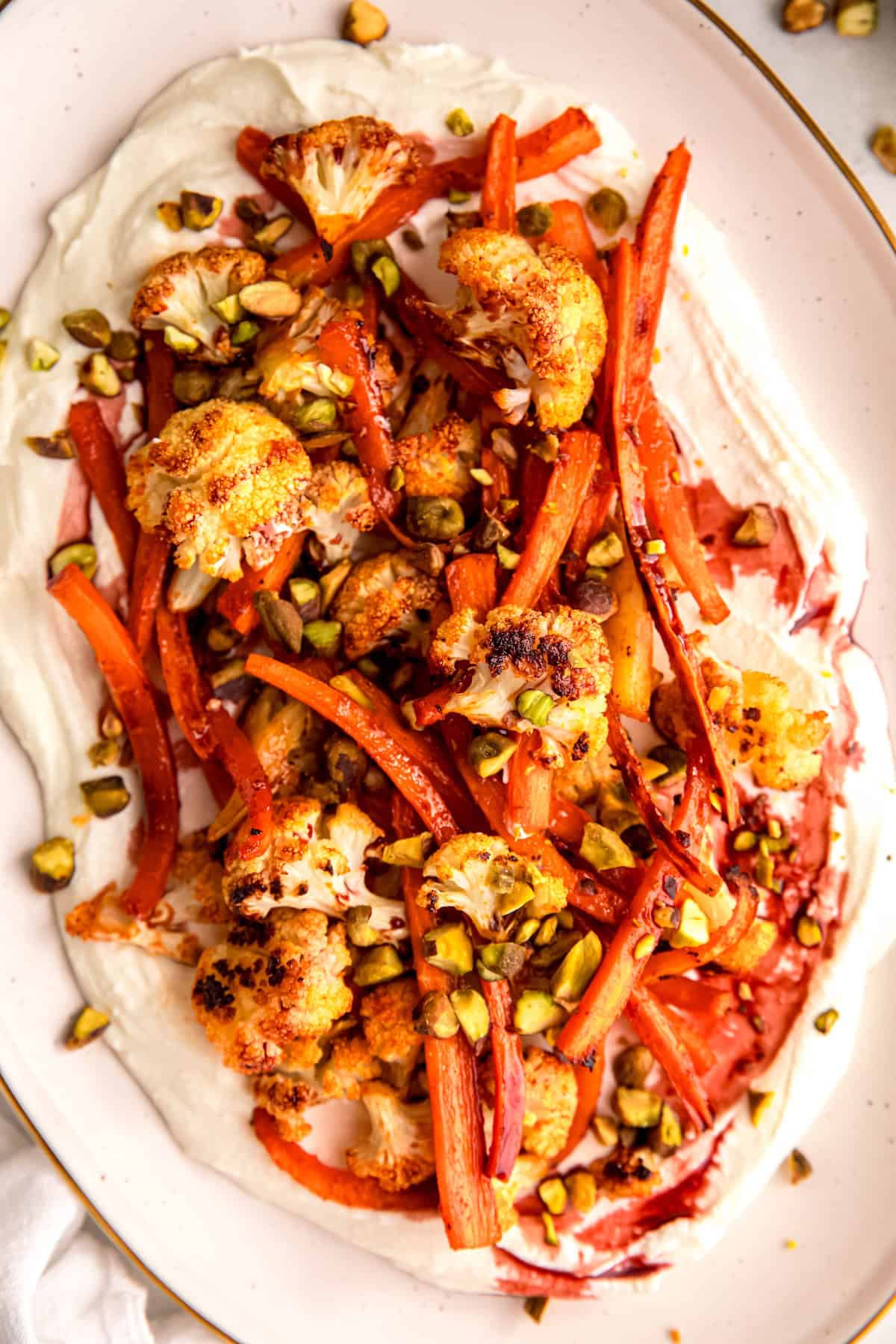 closeup overhead shot of a serving platter of harissa roasted carrots and cauliflower with whipped feta, pistachios and pomegranate molasses.